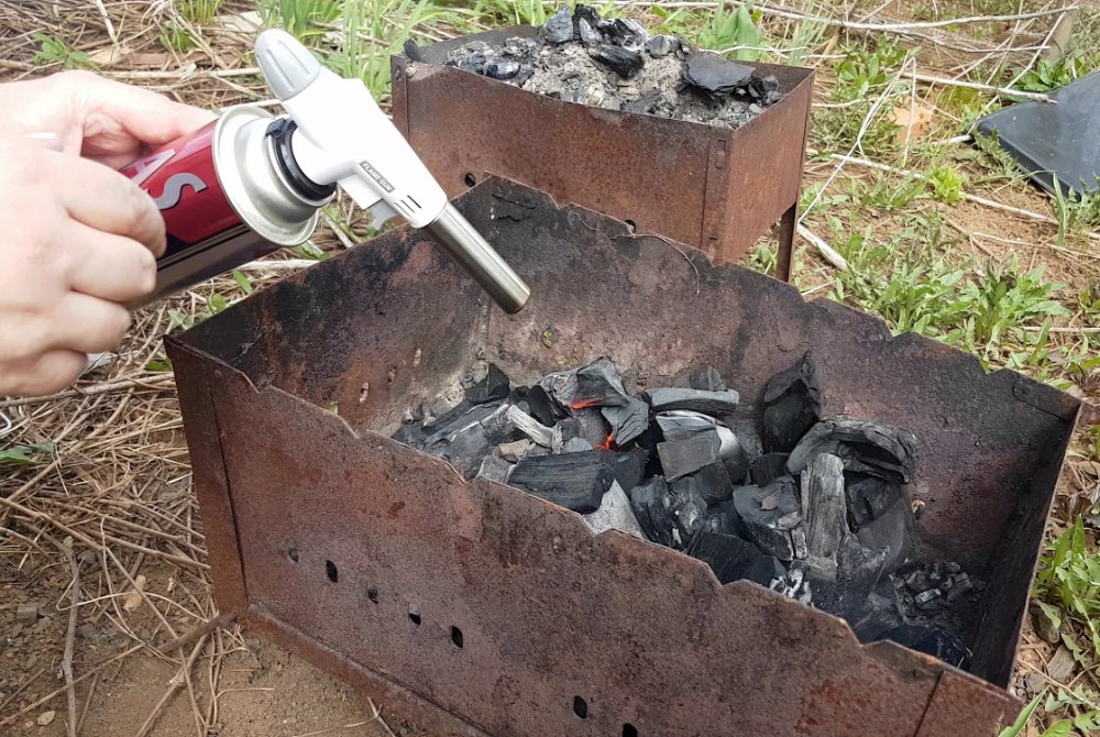 Человек разжигает угли с помощью газовой горелки