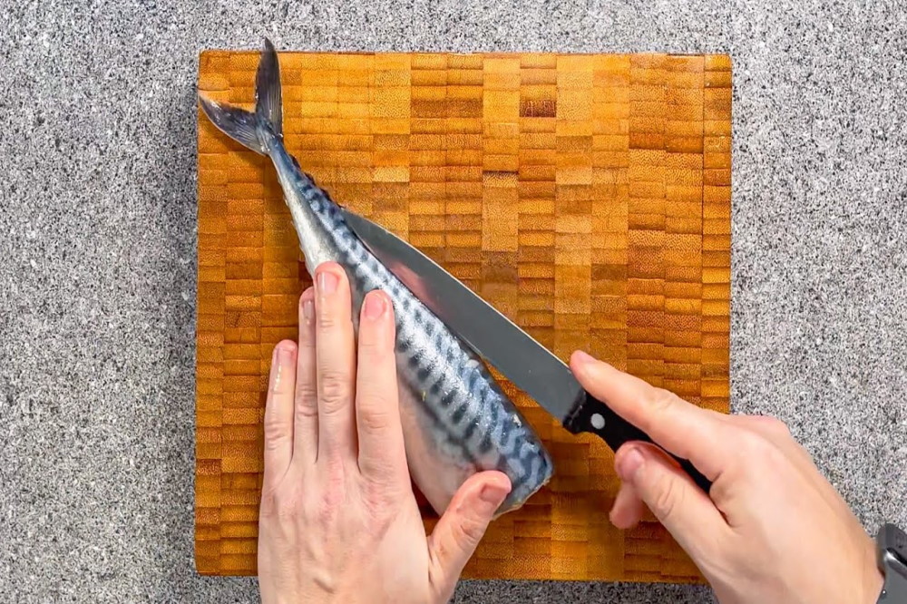 Повар ножом на деревянной доске разделывает скумбрию