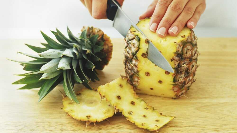 Человек отрезает ножом кожуру ананаса