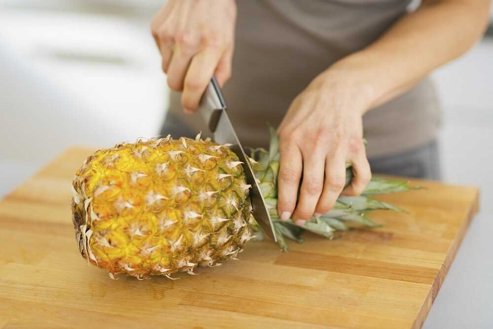 Человек срезает ножом верхушку ананаса