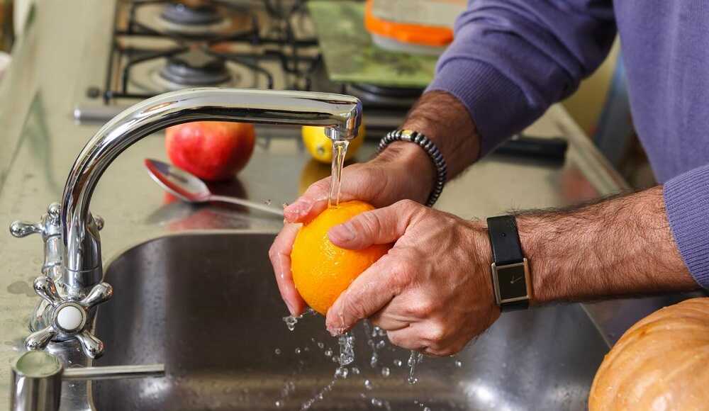 Мужчина моет апельсин под краном